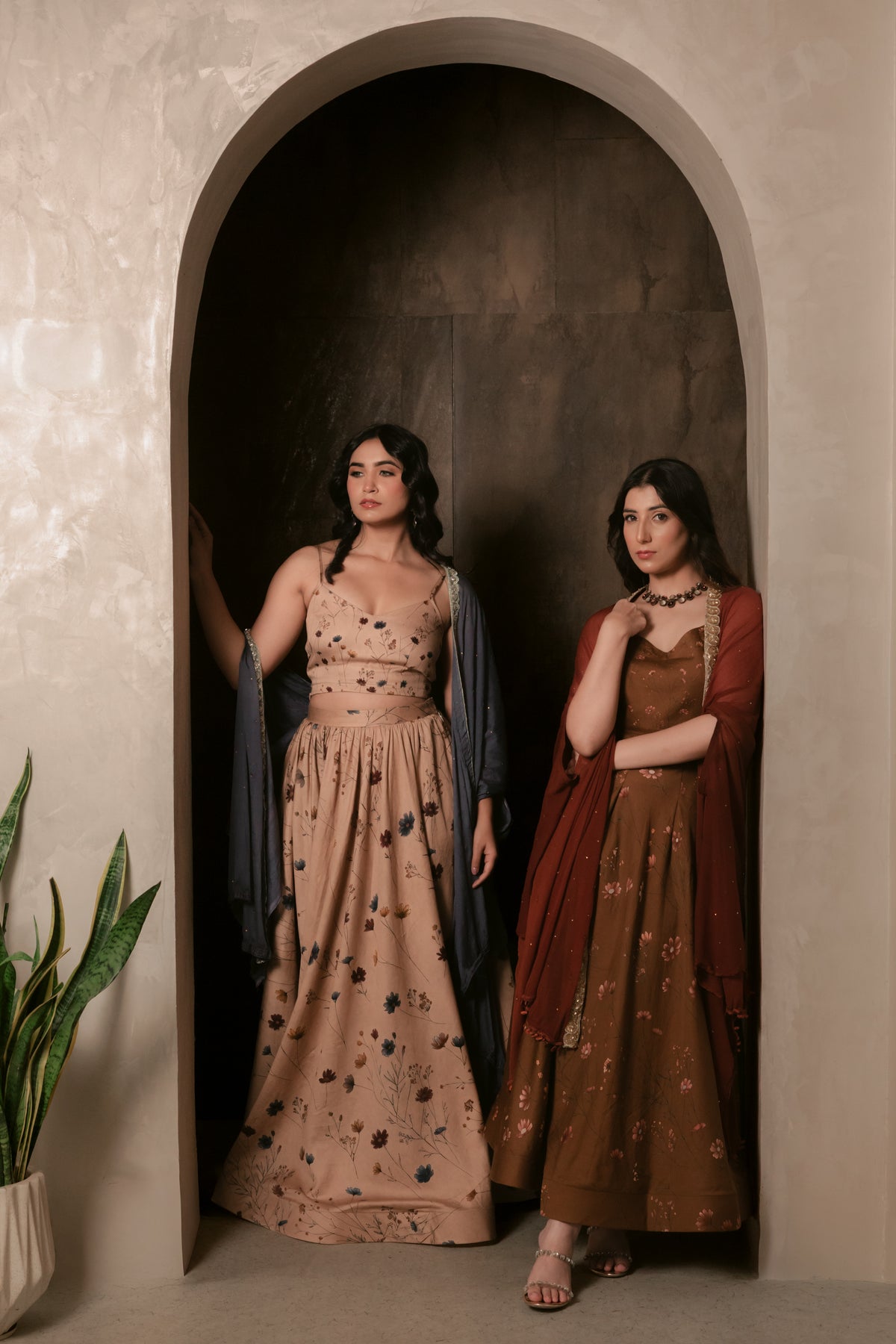 Two models wearing the Larkspur and Zinnia sets from the Sthira collection, standing in an arched doorway