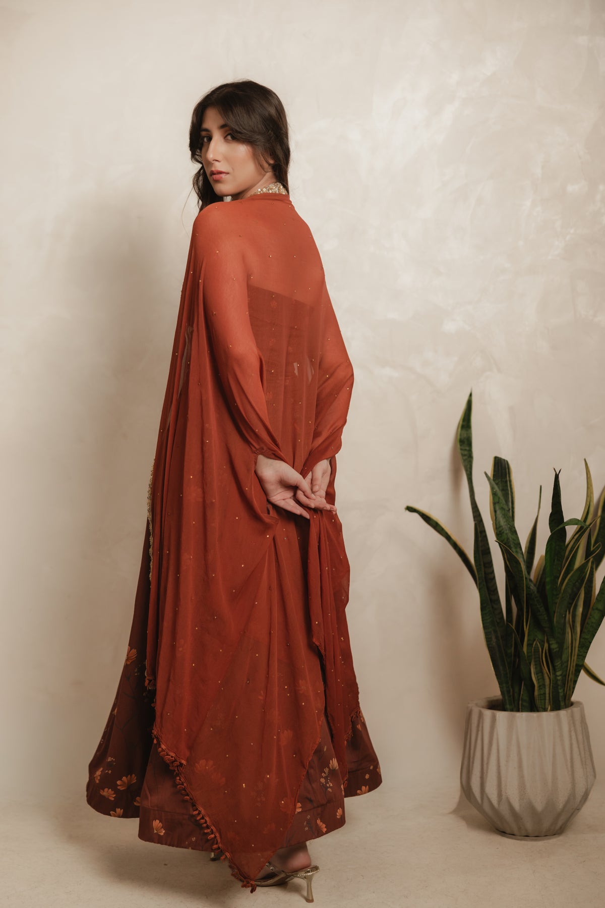 Sthira Calendula gown in vegan silk, rust-brown botanical print, back view with cape dupatta, looking over shoulder
