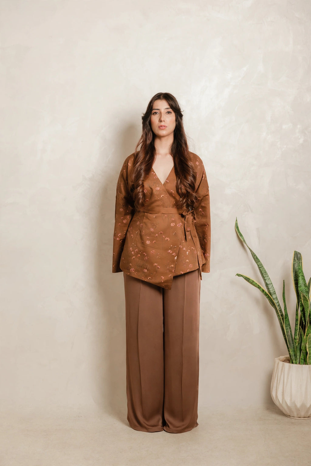 Sthira Primrose wrap top in rust brown with botanical print, worn with bronze-brown trousers