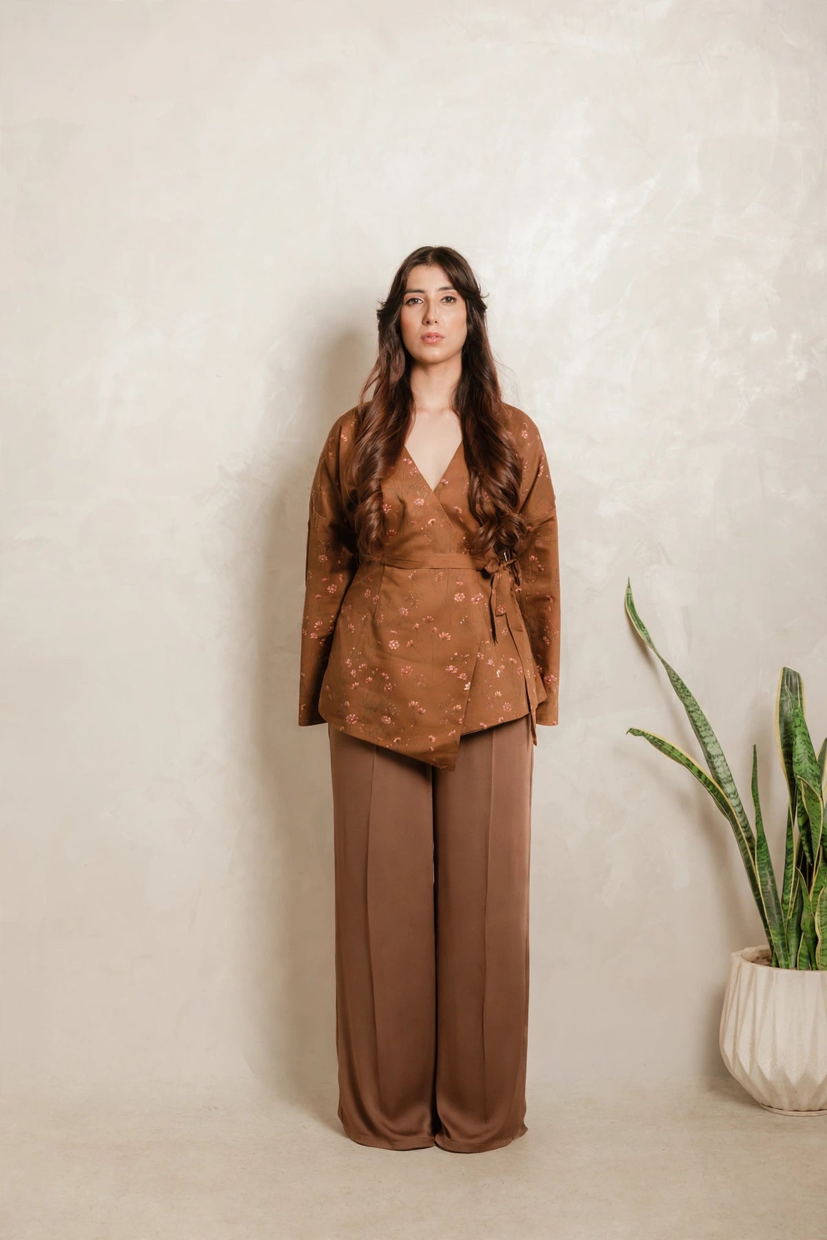 Sthira Primrose wrap top in rust brown with botanical print, worn with bronze-brown trousers