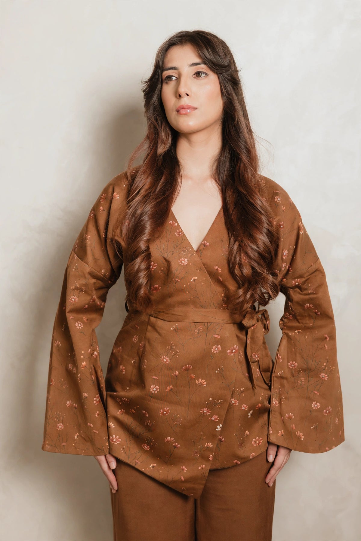 Sthira Primrose wrap top in rust brown with botanical print, worn with bronze-brown trousers